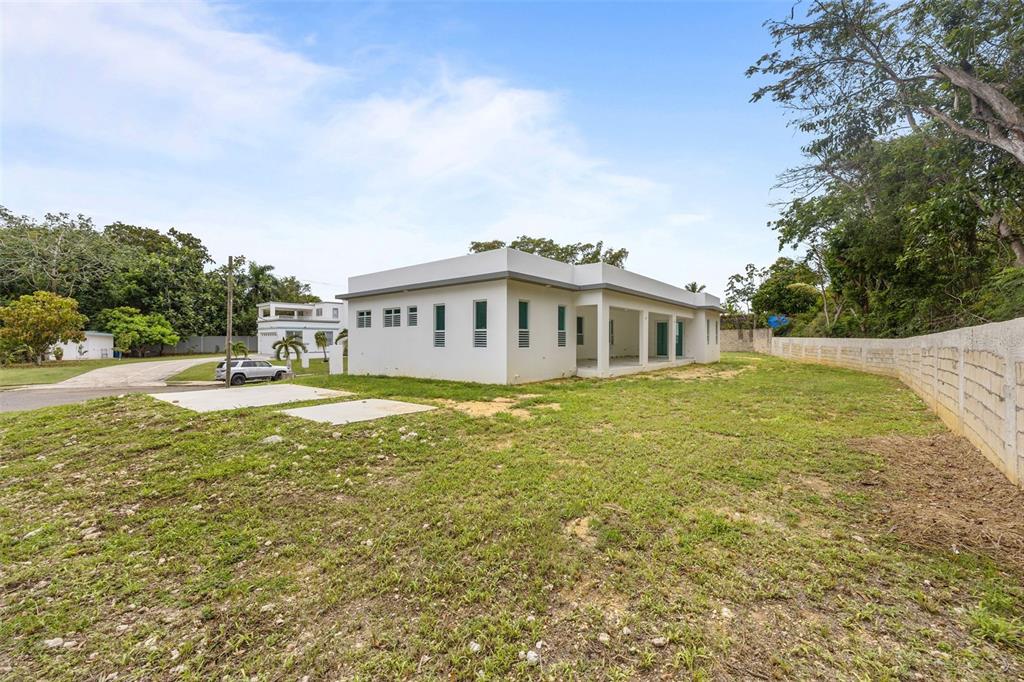 A white, single-story house with a flat roof sits on a large, grassy lot — solar 2 villa alemeria MARCEL, AGUADILLA, PR