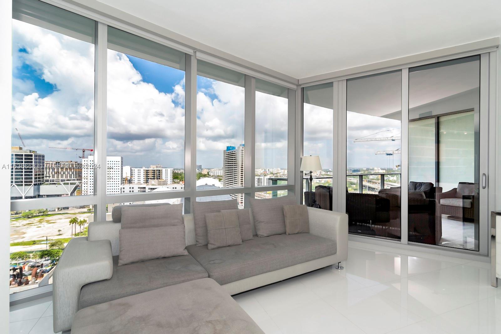 A living room with a grey sectional sofa, white tile floors, and floor-to-ceiling windows — 851 NE 1st Ave # 1710, Miami FL 33132, MIAMI, FL