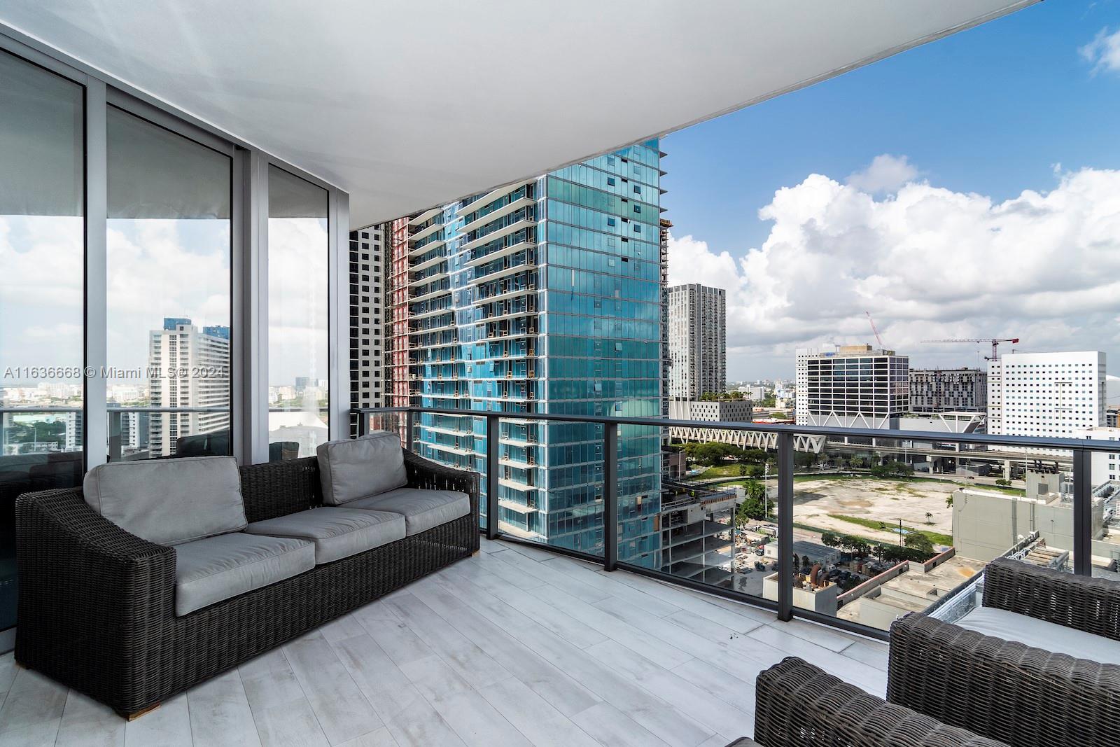 A balcony with wicker furniture overlooks a city skyline with several high-rise buildings — 851 NE 1st Ave # 1710, Miami FL 33132, MIAMI, FL