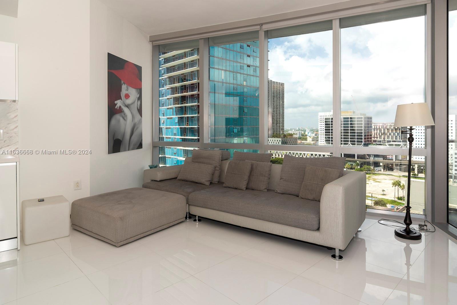 A modern living room features a gray sectional sofa, white tile floors, and floor-to-ceiling windows — 851 NE 1st Ave # 1710, Miami FL 33132, MIAMI, FL