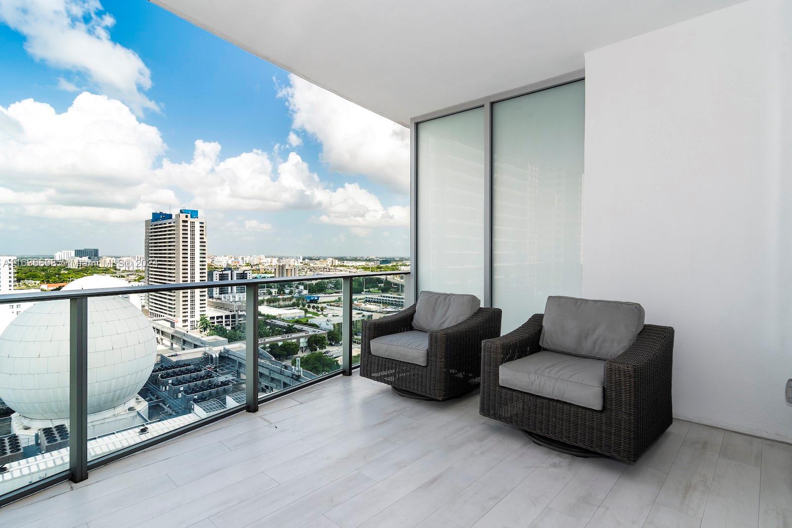 A balcony with two wicker armchairs overlooks a city skyline and a large white dome — 851 NE 1st Ave # 1710, Miami FL 33132, MIAMI, FL