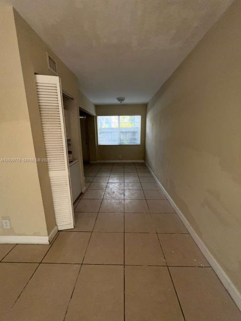 A narrow room with beige walls and light-colored square floor tiles leads to a window — 4625 NW 9th Dr # 4625, Plantation FL 33317, PLANTATION, FL