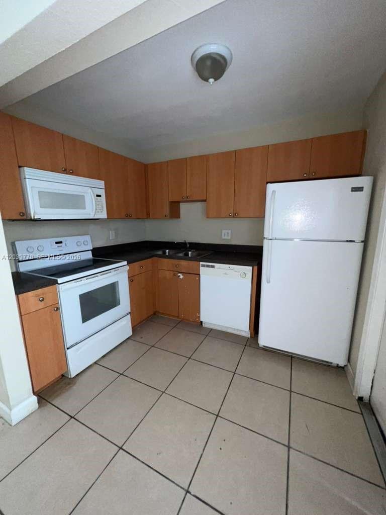 A kitchen features wood cabinets, white appliances, dark countertops, and light-colored tile flooring — 4625 NW 9th Dr # 4625, Plantation FL 33317, PLANTATION, FL