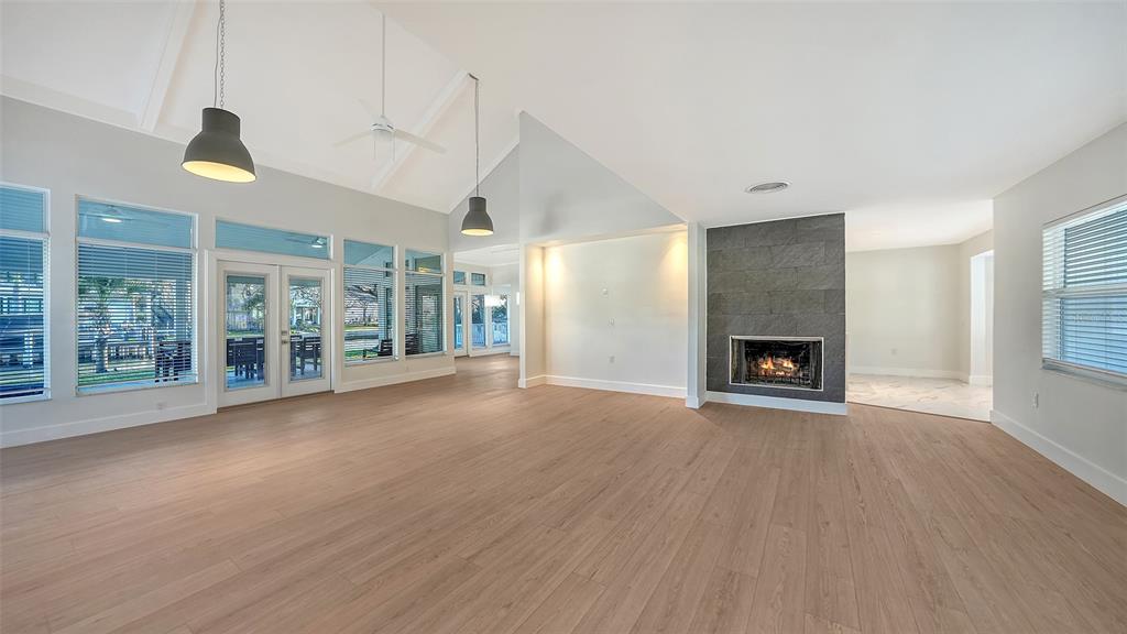 A spacious living room features light wood flooring, a stone fireplace, and large glass doors — 940 ALAMEDA WAY, SARASOTA, FL