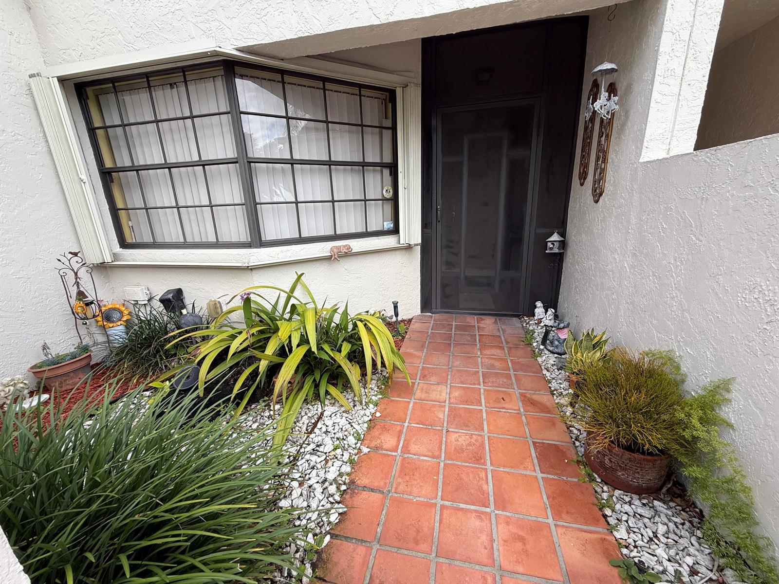 A tiled walkway leads to a front door with a screen door beside a bay window — 5878 Parkwalk Circle W, Boynton Beach FL 33472, BOYNTON BEACH, FL