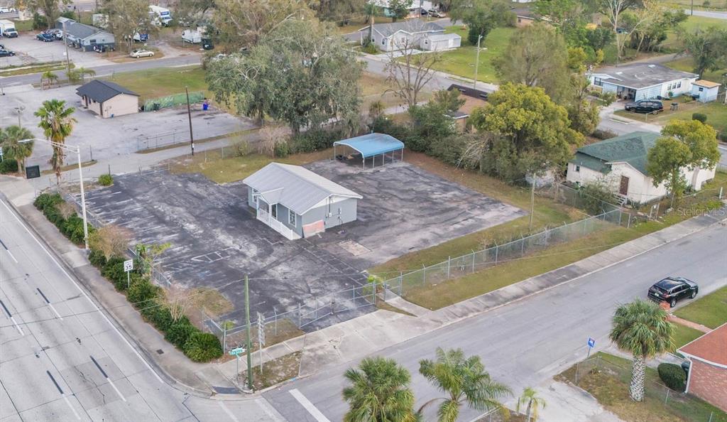An aerial view shows a small grey building situated on a large, paved fenced lot — 214 W MEMORIAL BOULEVARD, LAKELAND, FL