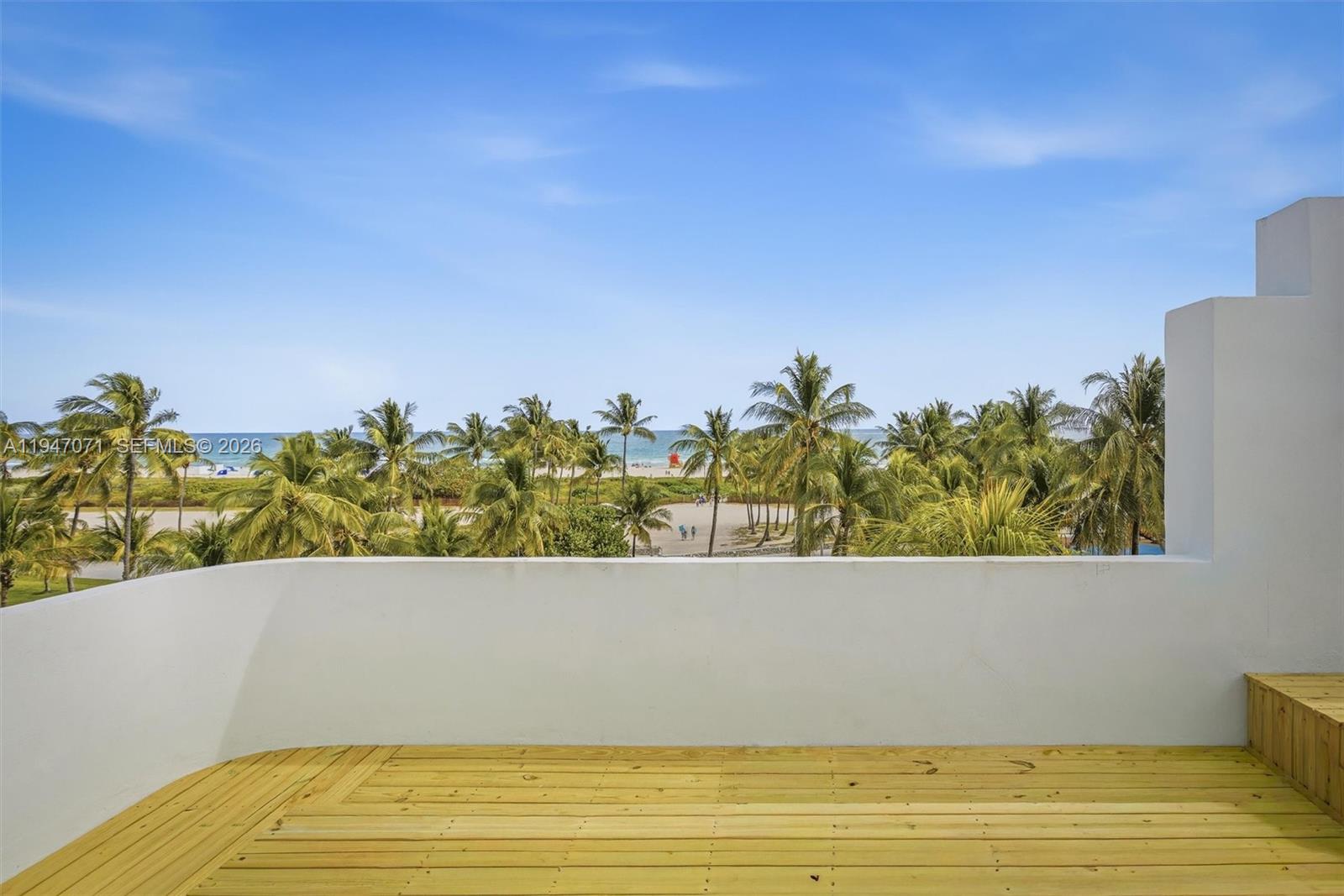 A wooden deck overlooks a beach with palm trees under a clear blue sky — 1250 Ocean Dr, Miami Beach FL 33139, MIAMI BEACH, FL