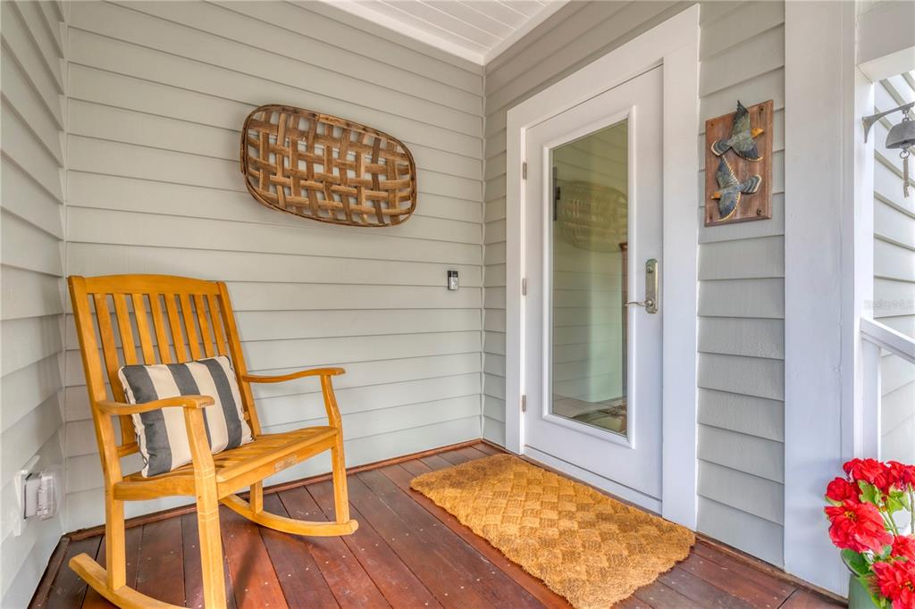 A wooden rocking chair sits on a covered porch with light gray siding and a door — 367 NIGHT HERON DRIVE, BOCA GRANDE, FL