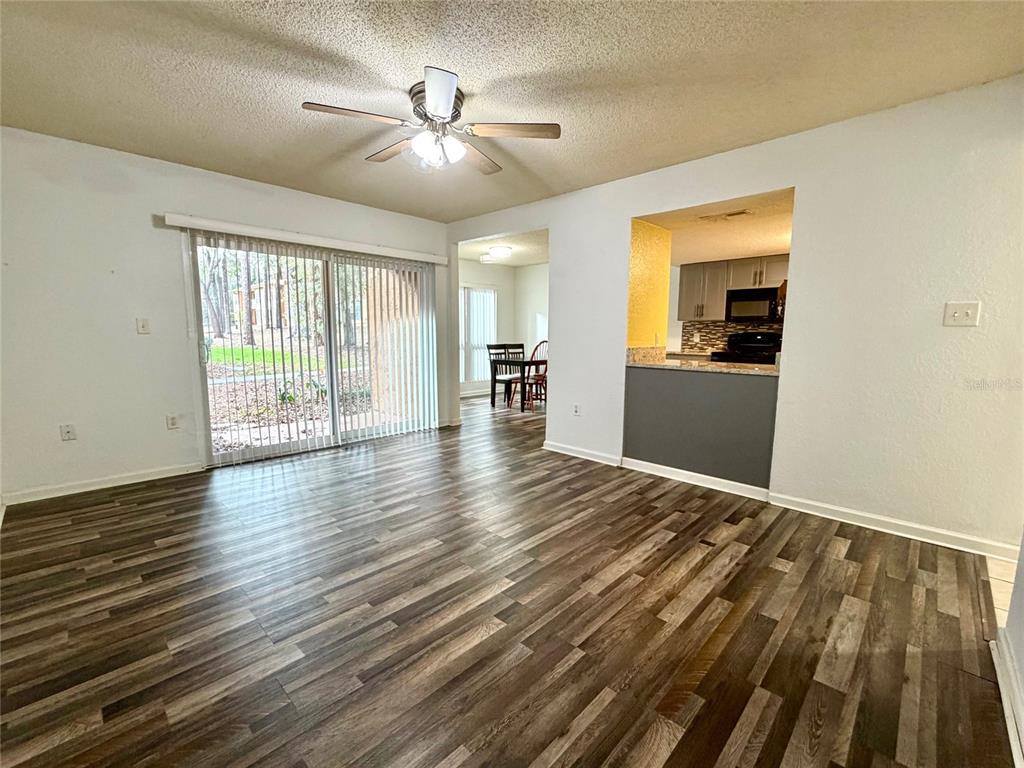 A living room with wood-look flooring, a ceiling fan, and a sliding glass door — 1810 NW 23RD BOULEVARD UNIT 180, GAINESVILLE, FL