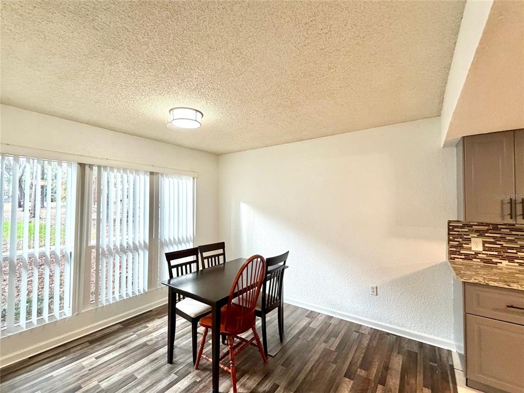 A dining area features wood-look flooring, a dark table with chairs, and vertical window blinds — 1810 NW 23RD BOULEVARD UNIT 180, GAINESVILLE, FL