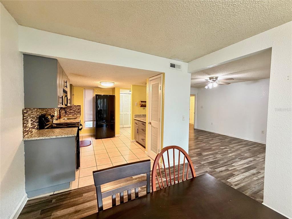 A kitchen with grey cabinets and a black refrigerator opens into a dining area — 1810 NW 23RD BOULEVARD UNIT 180, GAINESVILLE, FL