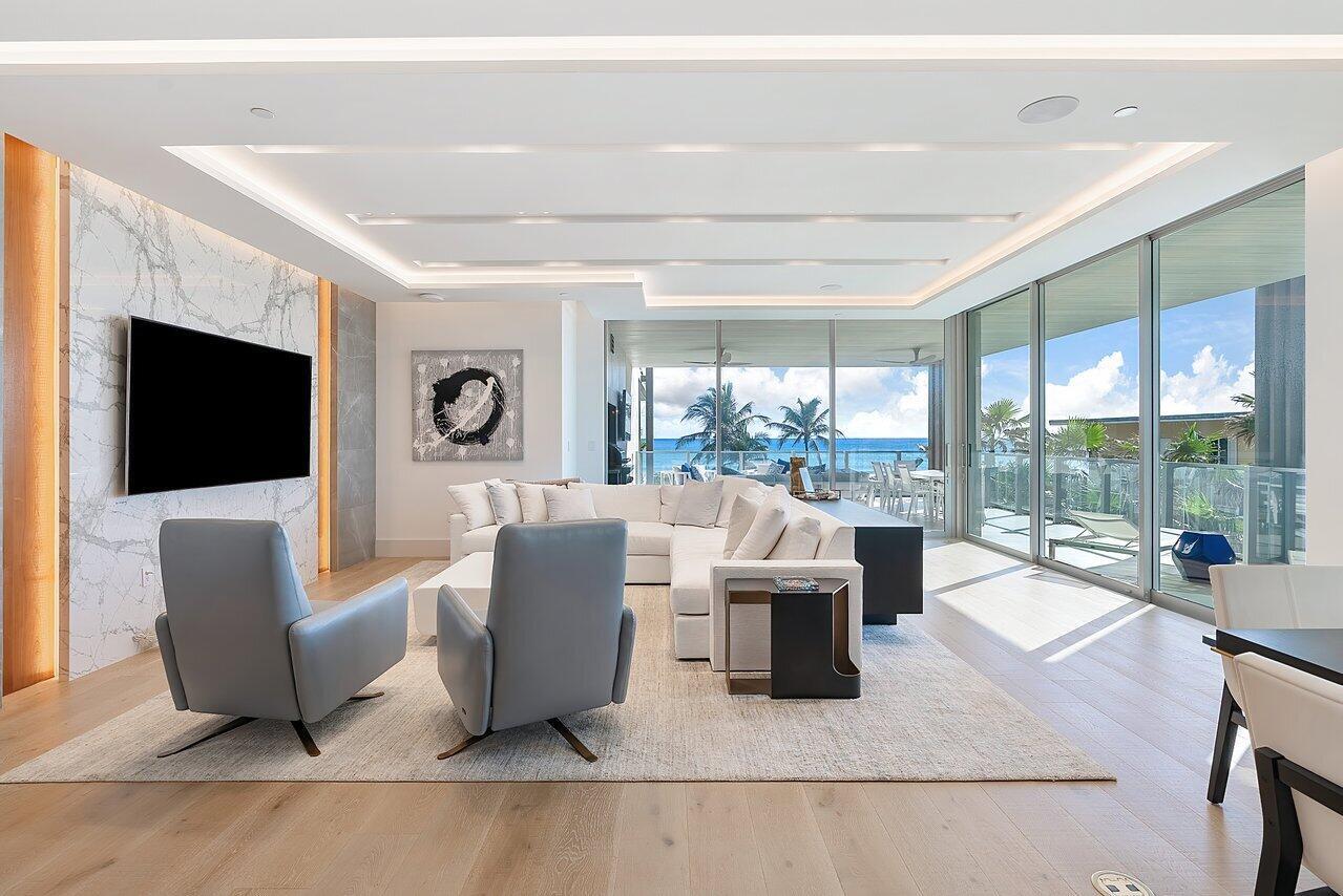 A modern living room features a marble accent wall, grey armchairs, and floor-to-ceiling ocean views — 1901 S Ocean Boulevard # 10, Delray Beach FL 33483, DELRAY BEACH, FL