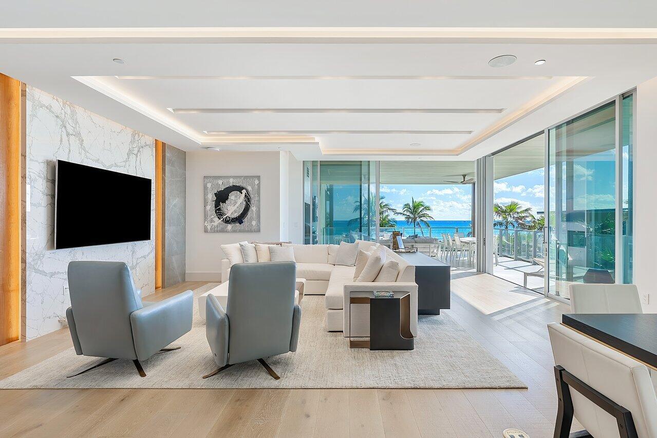 A modern living room features a marble accent wall, blue armchairs, and floor-to-ceiling ocean views — 1901 S Ocean Boulevard # 10, Delray Beach FL 33483, DELRAY BEACH, FL