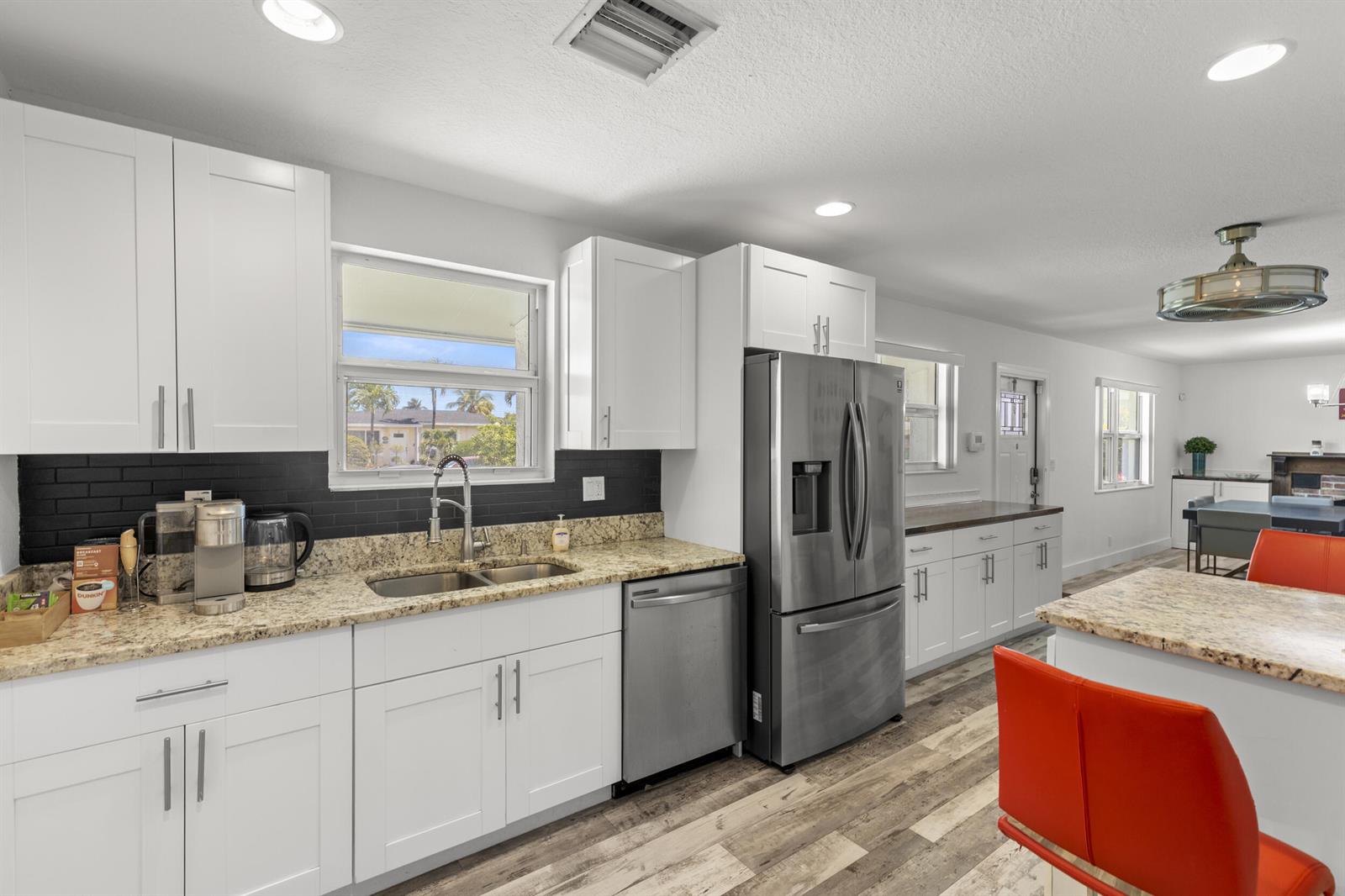 A kitchen features white cabinets, granite countertops, a stainless steel refrigerator, and wood-look flooring — 944 Hansen Street, West Palm Beach FL 33405, WEST PALM BEACH, FL