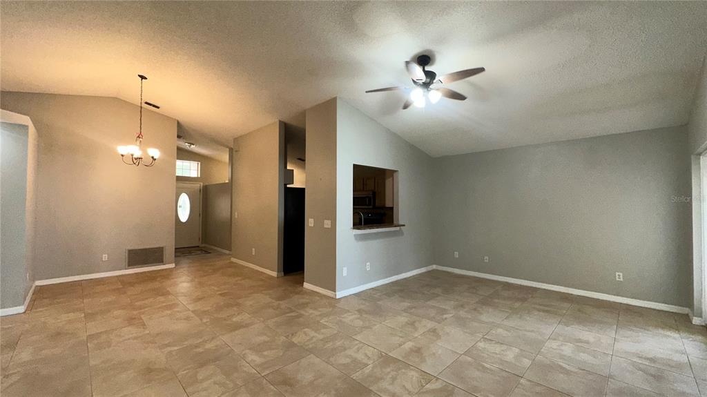An open-concept living and dining area features light tile flooring and a vaulted ceiling — 2429 SAPIER COURT, ORLANDO, FL