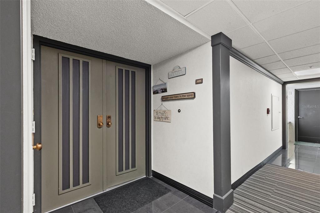 A hallway features a double-door entrance with gray panels, decorative wall signs, and tiled flooring — 1480 GULF BOULEVARD UNIT 409, CLEARWATER BEACH, FL