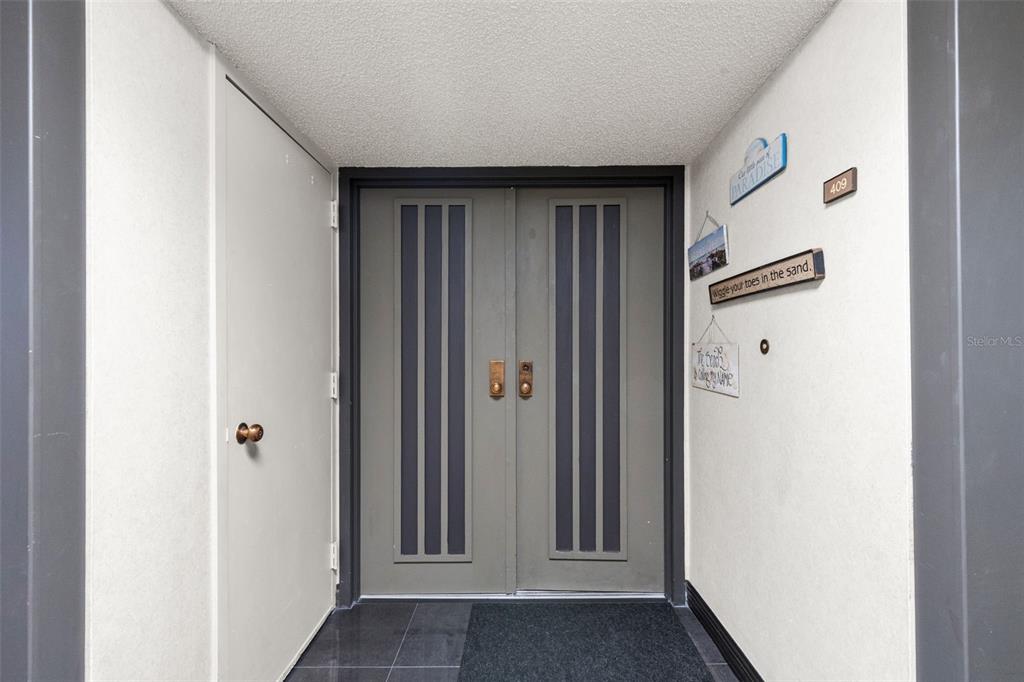 A gray double door entrance with a side door and decorative wall signs — 1480 GULF BOULEVARD UNIT 409, CLEARWATER BEACH, FL
