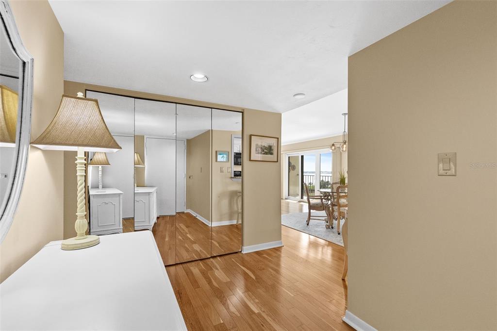 A hallway with hardwood floors and mirrored closet doors leads to a dining area — 1480 GULF BOULEVARD UNIT 409, CLEARWATER BEACH, FL