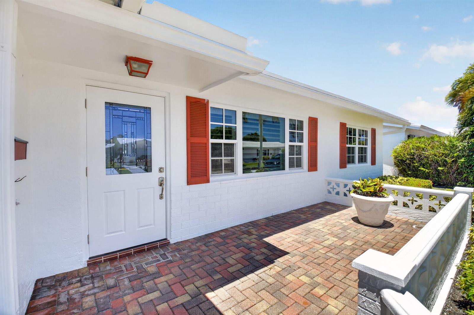 A white house exterior features a brick patio, red shutters, and a front door — 1709 SW 20th Street, Boynton Beach FL 33426, BOYNTON BEACH, FL