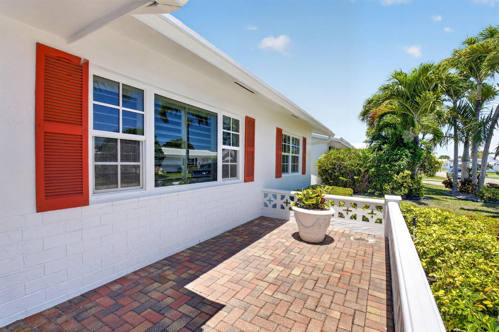 A white brick house exterior features orange shutters, a brick patio, and a decorative wall — 1709 SW 20th Street, Boynton Beach FL 33426, BOYNTON BEACH, FL