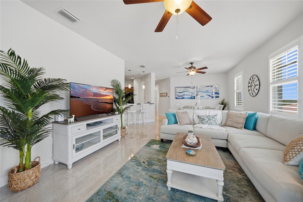 A bright living room features a white sectional sofa, a television console, and a ceiling fan — 17288 ACAPULCO ROAD UNIT 421, PUNTA GORDA, FL