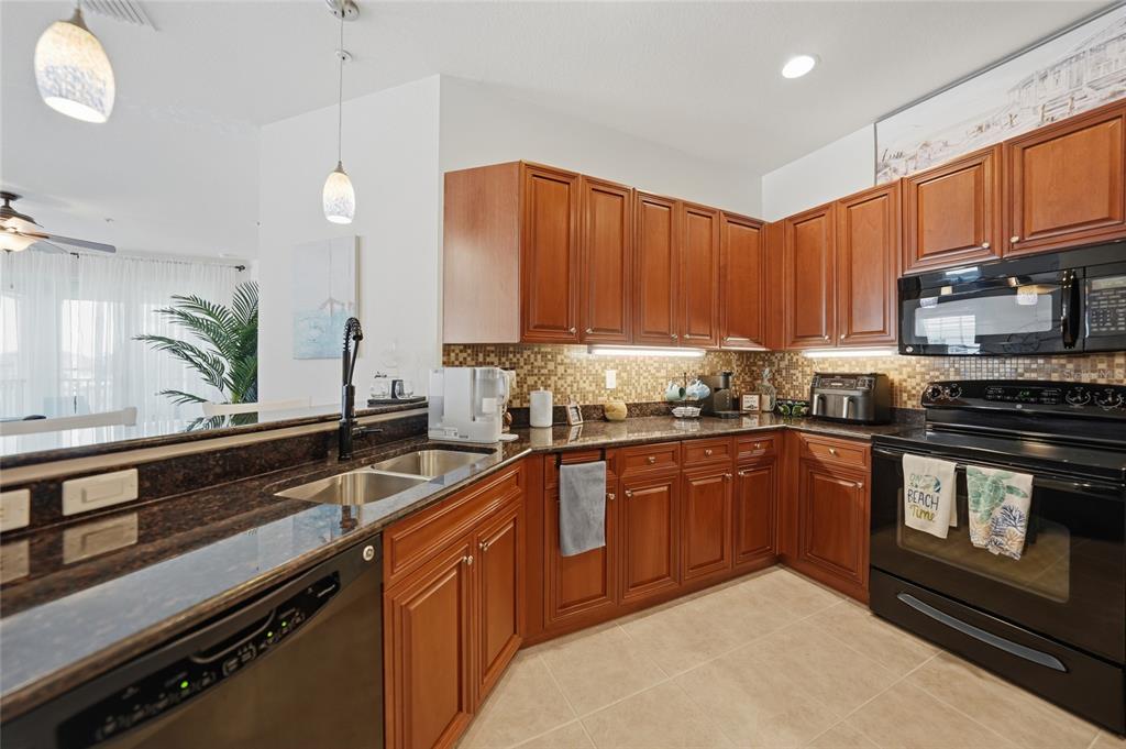 A kitchen features wood cabinets, dark granite countertops, a tile backsplash, and black appliances — 17288 ACAPULCO ROAD UNIT 421, PUNTA GORDA, FL