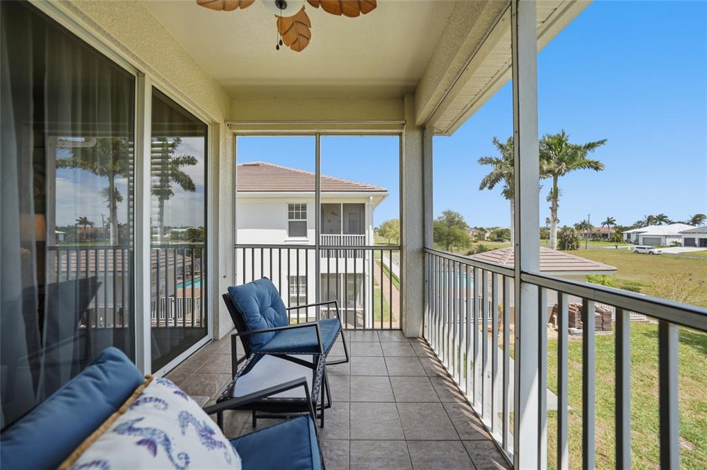 A screened-in balcony features tiled flooring, two blue chairs, and a view of neighboring buildings — 17288 ACAPULCO ROAD UNIT 421, PUNTA GORDA, FL
