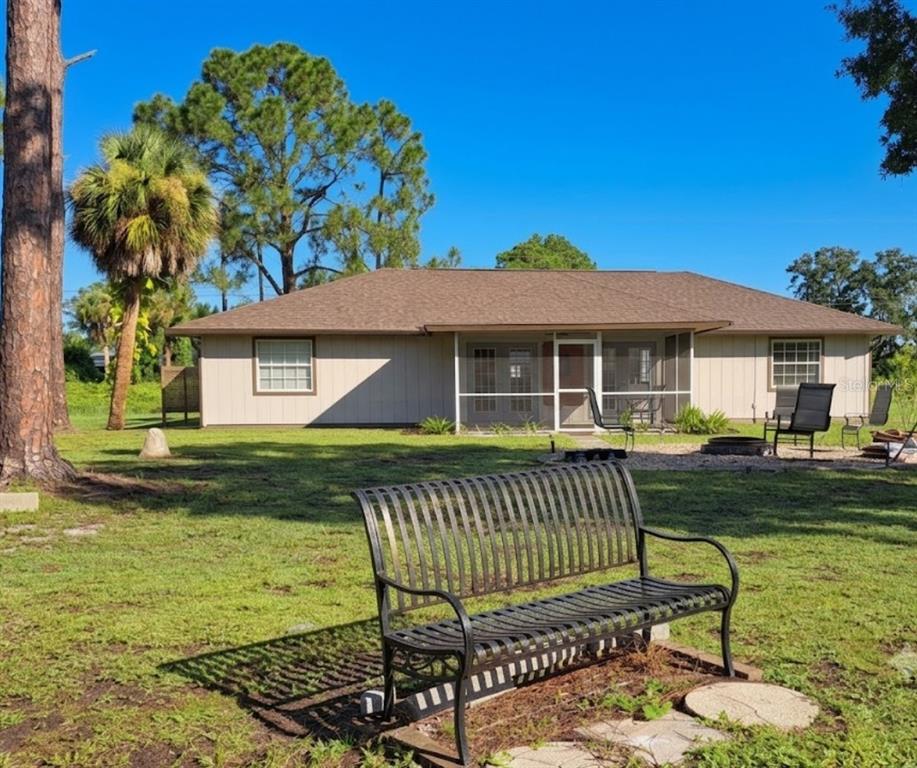 A metal bench sits in a grassy backyard facing a single-story house with a screened porch — 3331 TRAVERSE AVENUE, NORTH PORT, FL