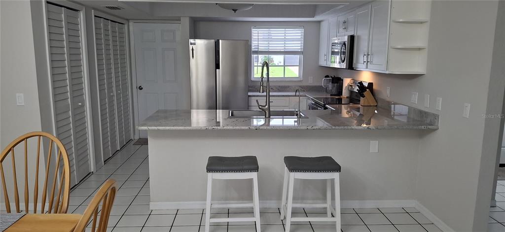 A kitchen features white cabinets, granite countertops, stainless steel appliances, and two bar stools — 3331 TRAVERSE AVENUE, NORTH PORT, FL
