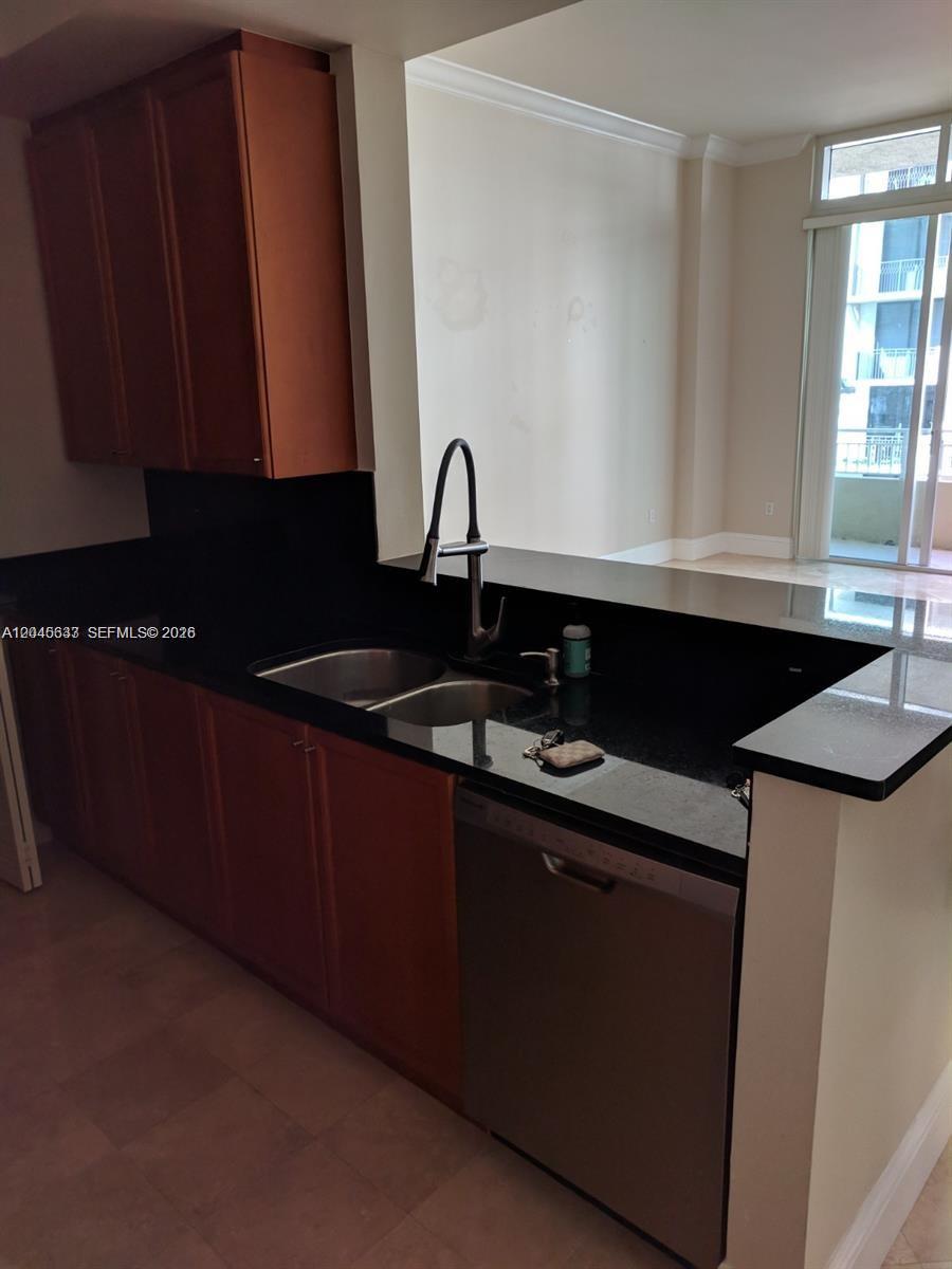 A kitchen features dark wood cabinets, black countertops, a stainless steel dishwasher, and a sink — 99 SE Mizner Blvd # 537, Boca Raton FL 33432, BOCA RATON, FL