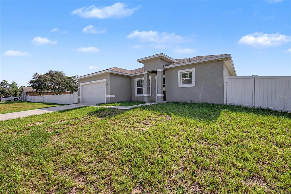 A single-story house with a gray stucco exterior, a white garage door, and a white fence — 17199 SW 43RD COURT, OCALA, FL