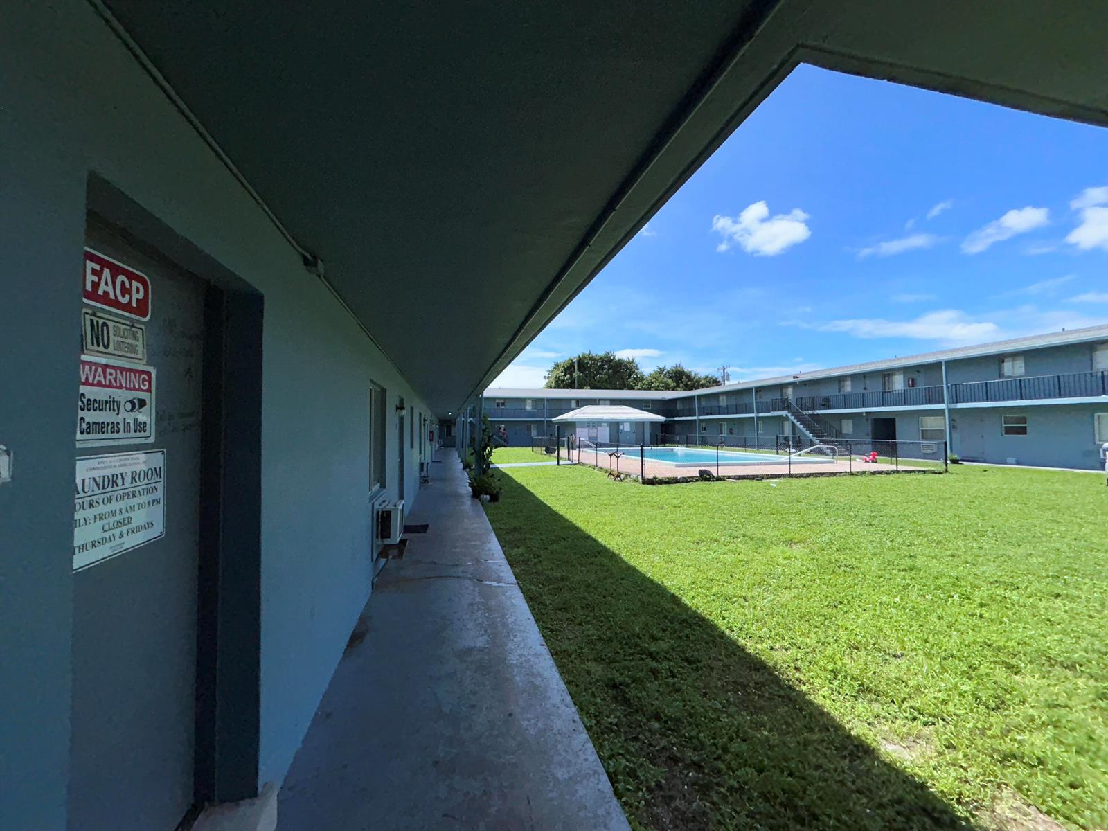 An outdoor walkway overlooks a grassy courtyard with a fenced swimming pool at an apartment complex — 1829 N A Street # 65, FL 33460, FL