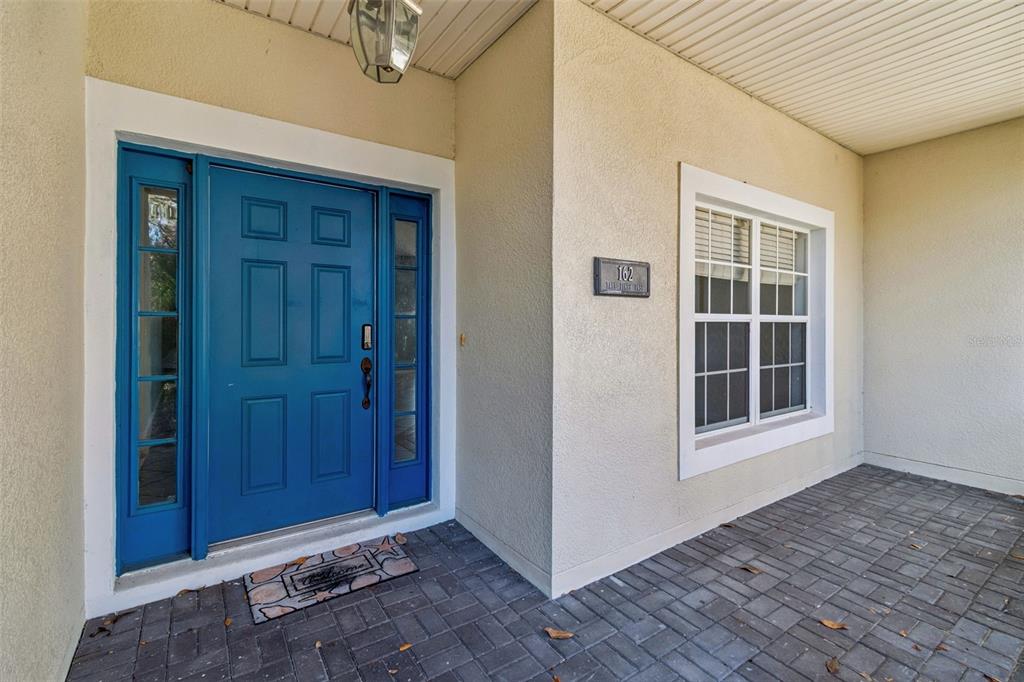 A blue front door with sidelights sits on a paved porch next to a window — 162 TALL PINES PASS, KISSIMMEE, FL