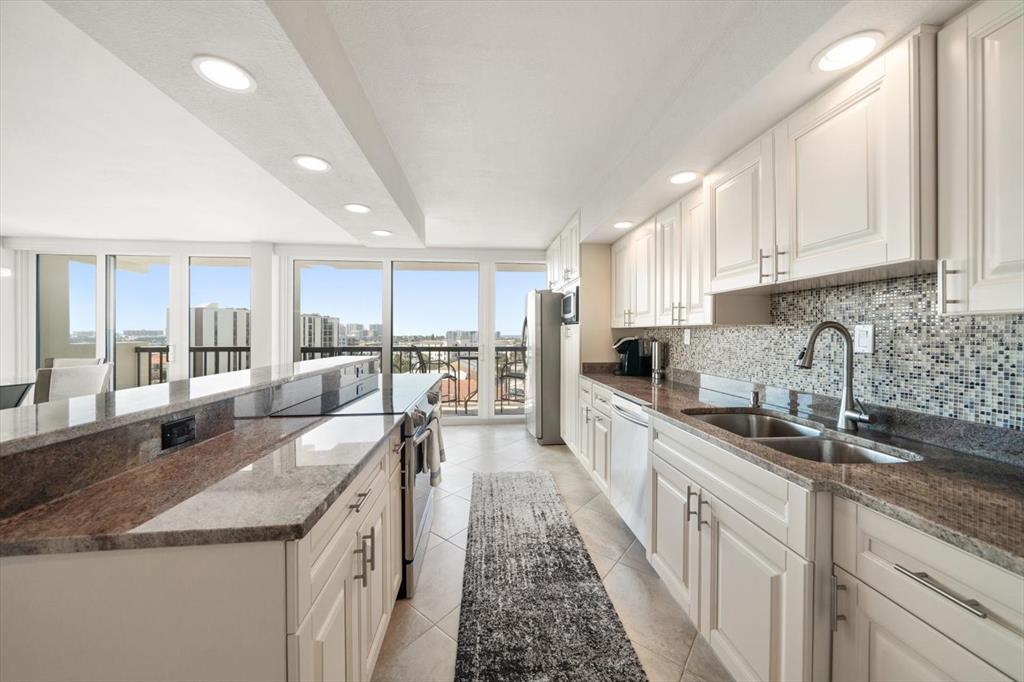 A kitchen features white cabinets, granite countertops, a mosaic tile backsplash, and floor-to-ceiling windows — 400 ISLAND WAY UNIT 901, CLEARWATER BEACH, FL