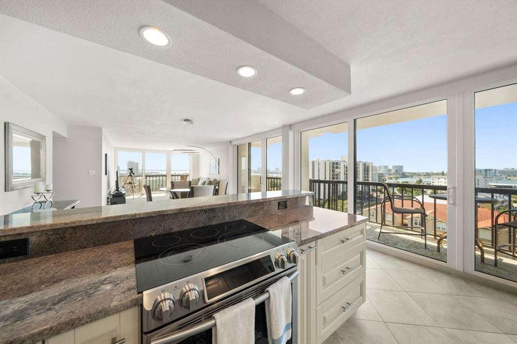 A kitchen with granite countertops and a glass-top stove overlooks a balcony and water view — 400 ISLAND WAY UNIT 901, CLEARWATER BEACH, FL