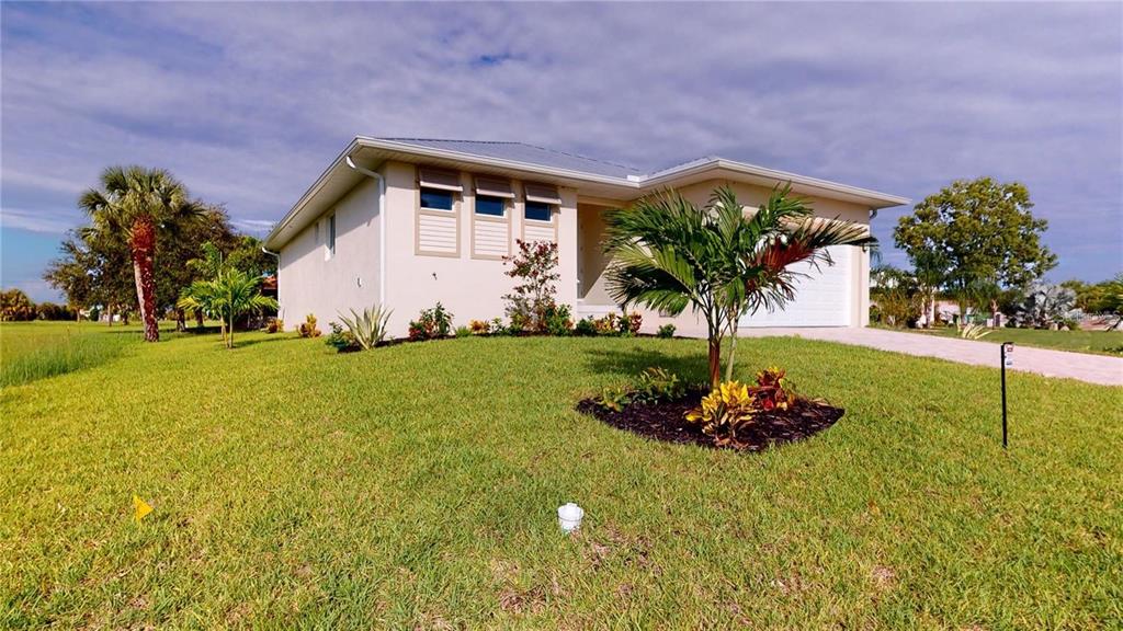 A single-story house with a light-colored exterior, a metal roof, and a landscaped front yard — 17007 GINGER LANE, PUNTA GORDA, FL