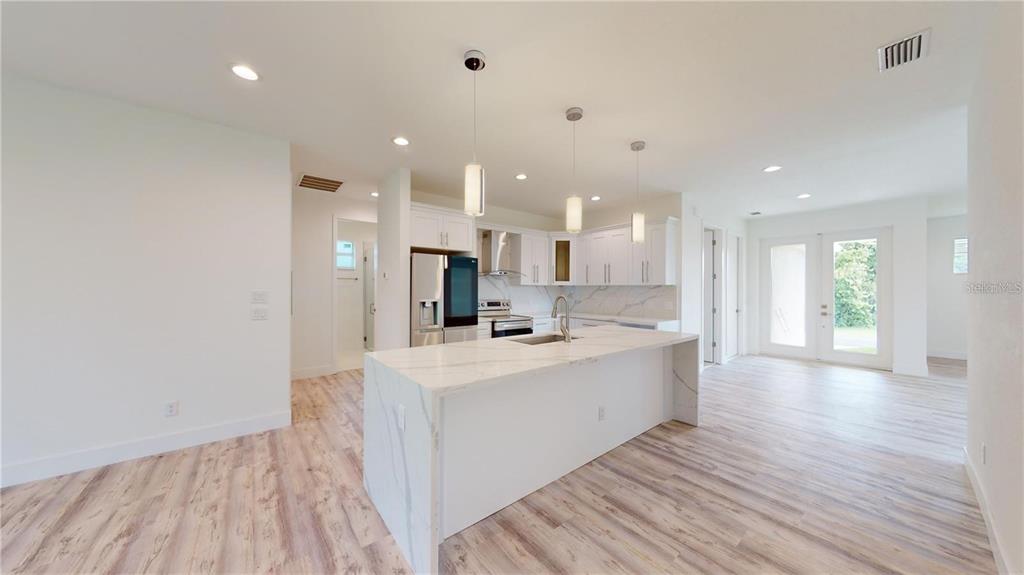 A modern kitchen features a marble-topped island, white cabinetry, and light wood-look flooring — 17007 GINGER LANE, PUNTA GORDA, FL