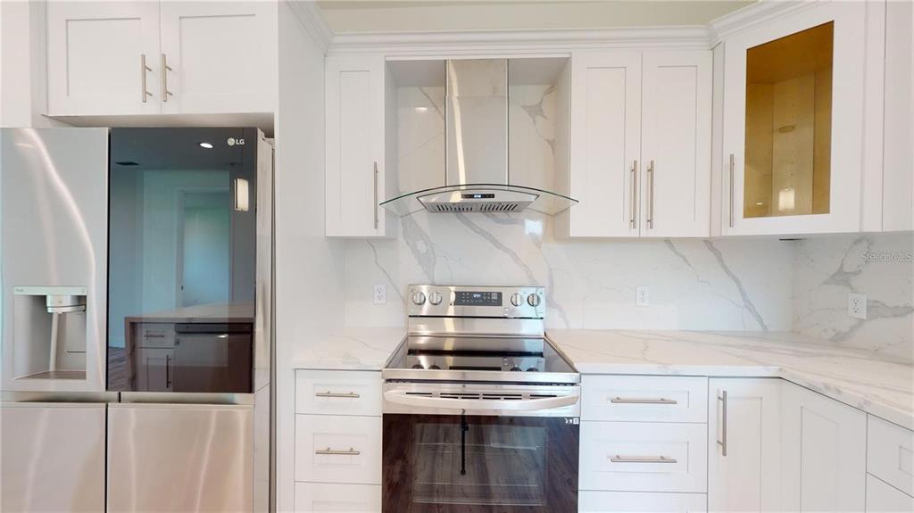 A modern kitchen features white shaker cabinets, marble-look countertops, stainless steel appliances, and a range hood — 17007 GINGER LANE, PUNTA GORDA, FL