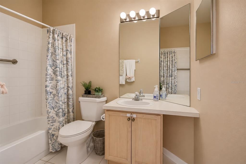 A bathroom features a vanity with a light wood cabinet, a mirror, and a shower-tub combo — 13560 TURTLE MARSH LOOP UNIT 338, ORLANDO, FL