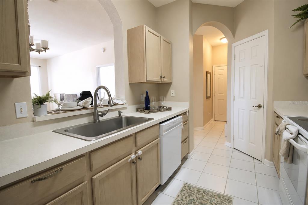 A kitchen features light wood cabinets, white countertops, a stainless steel sink, and white appliances — 13560 TURTLE MARSH LOOP UNIT 338, ORLANDO, FL
