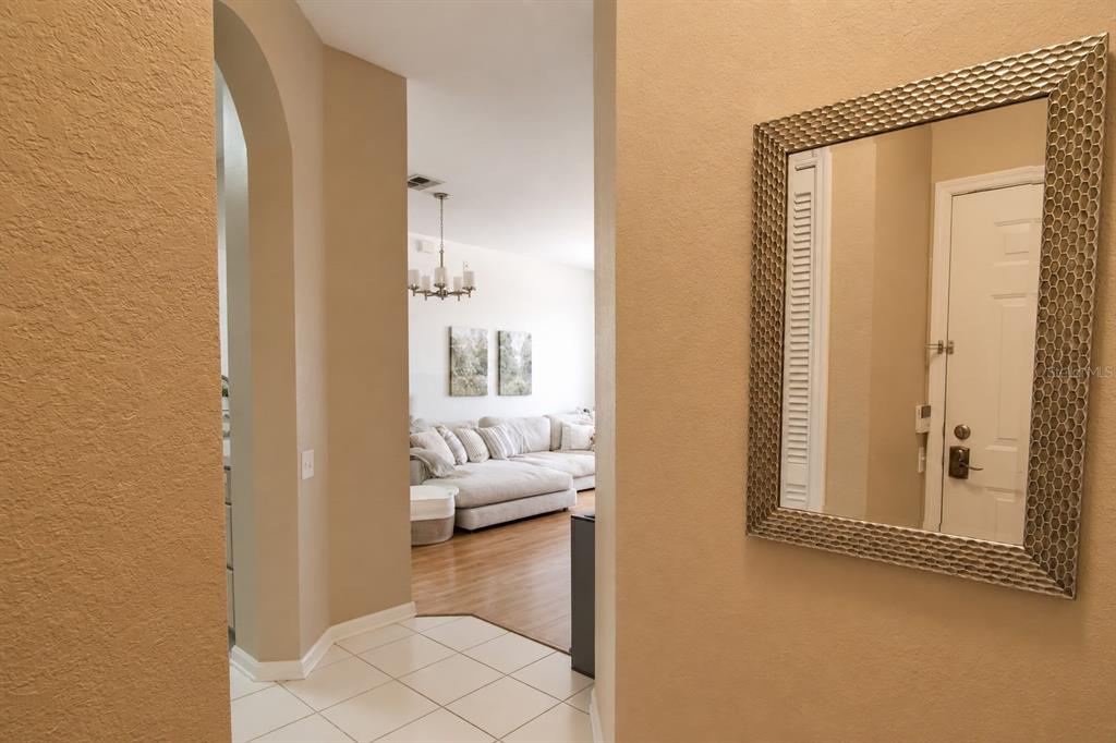 A hallway with tile flooring leads into a living room with a large sectional sofa — 13560 TURTLE MARSH LOOP UNIT 338, ORLANDO, FL