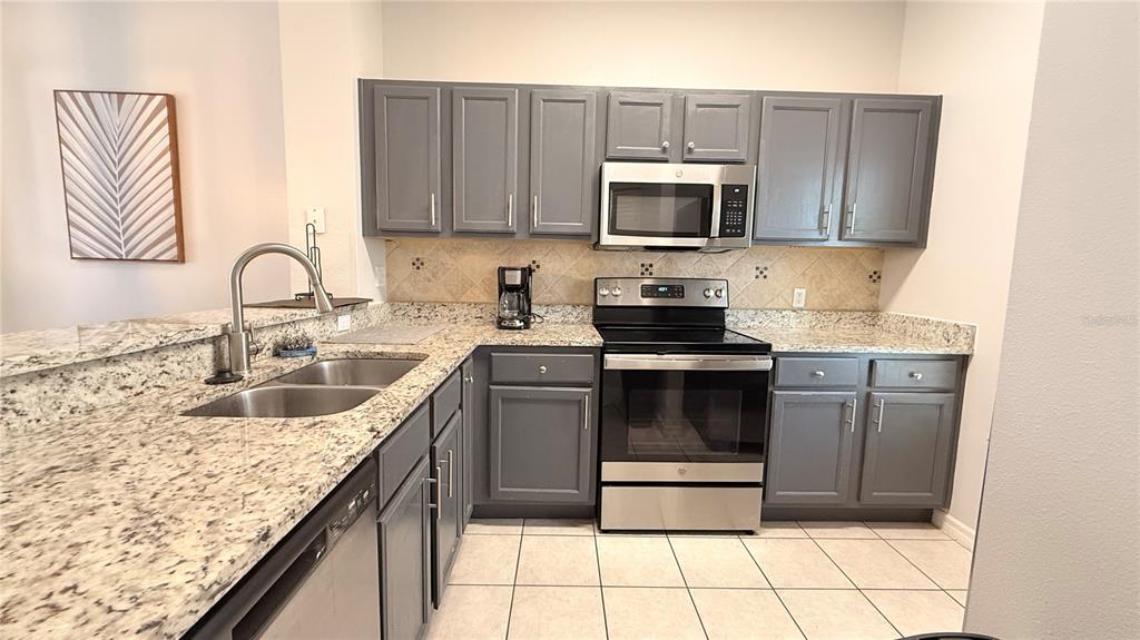 A kitchen features gray cabinets, granite countertops, stainless steel appliances, and a tile backsplash — 8517 BAY LILLY LOOP, KISSIMMEE, FL