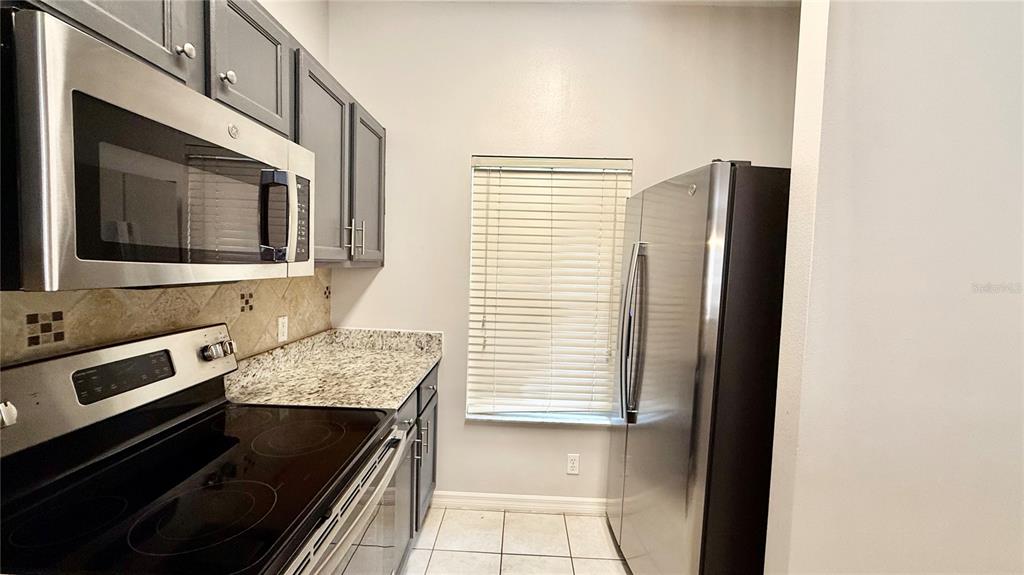 A kitchen features stainless steel appliances, dark gray cabinets, granite countertops, and tile flooring — 8517 BAY LILLY LOOP, KISSIMMEE, FL