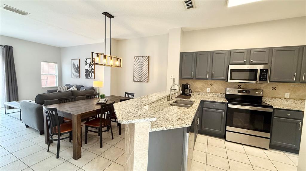 A kitchen with dark gray cabinets and granite countertops opens to a dining and living area — 8517 BAY LILLY LOOP, KISSIMMEE, FL