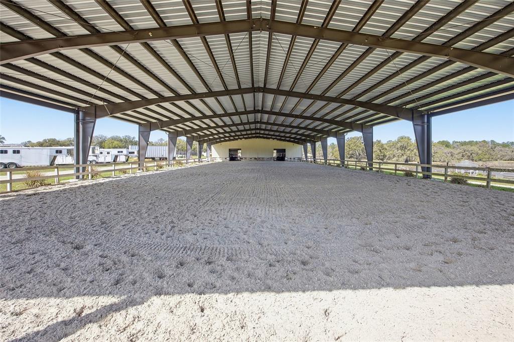 An open-air covered riding arena features a sand surface and metal structural framing — 6025 NW 115TH AVENUE, OCALA, FL
