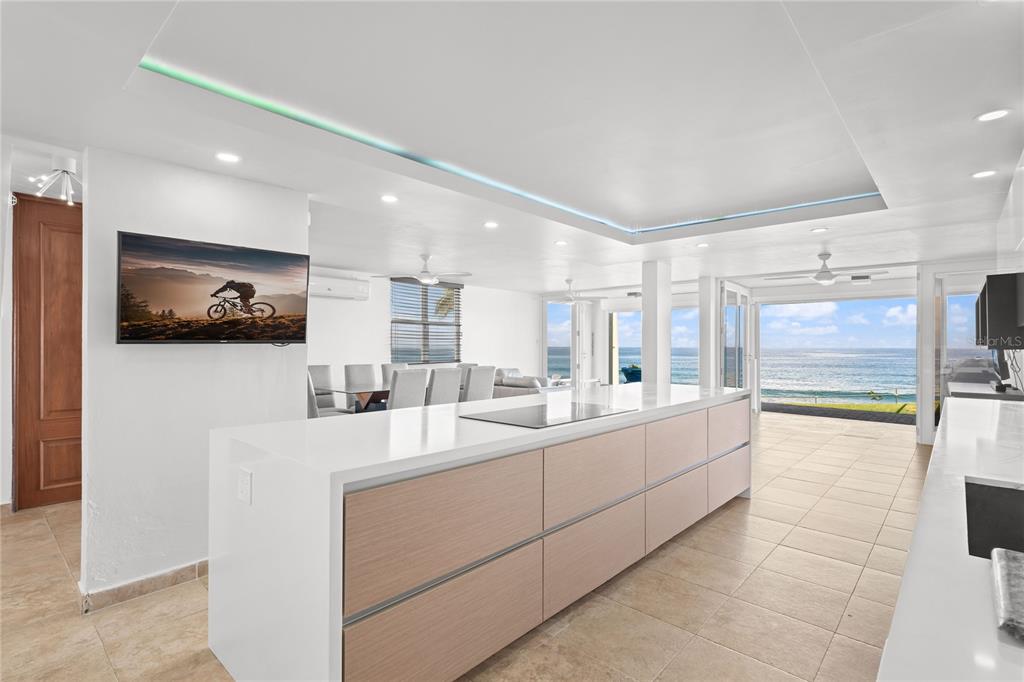 A modern kitchen with a large white island overlooks the ocean through open glass doors — J1 CALLE COSTA DORADA, DORADO, PR