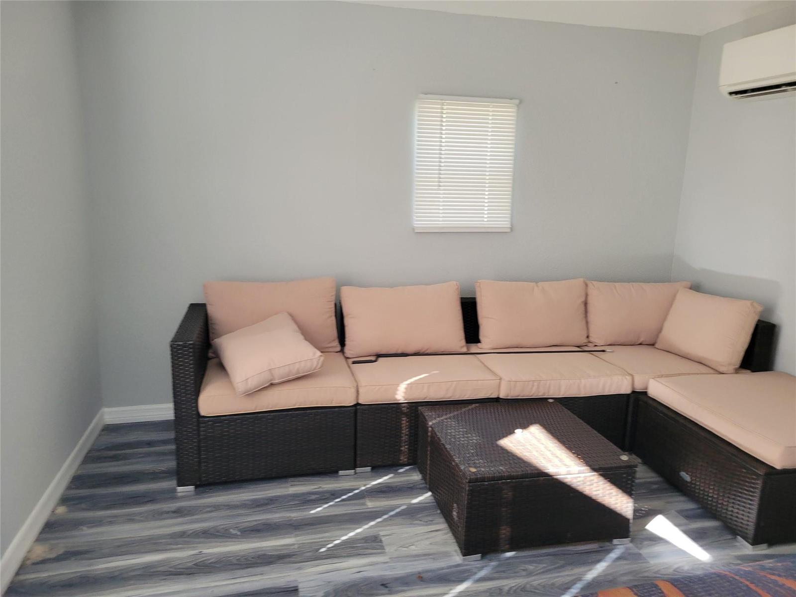 A room with gray walls, wood-look flooring, a window with blinds, and a modular wicker sofa — 3528 SW 7th Manor, Okeechobee FL 34974, OKEECHOBEE, FL