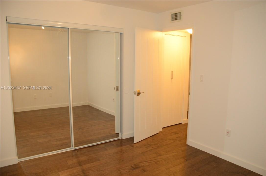 A bedroom features wood-look flooring, a mirrored sliding closet, and an open doorway — 937 Michigan Ave # 3, Miami Beach FL 33139, MIAMI BEACH, FL