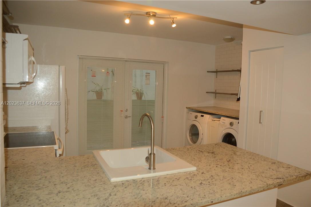 A kitchen features a granite island with a sink, white appliances, and laundry machines — 937 Michigan Ave # 3, Miami Beach FL 33139, MIAMI BEACH, FL