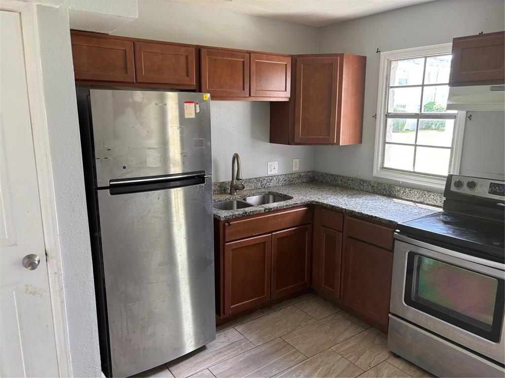 A kitchen features stainless steel appliances, wood cabinets, granite countertops, and light-colored tile flooring — 2779 L B MCLEOD ROAD UNIT A, ORLANDO, FL